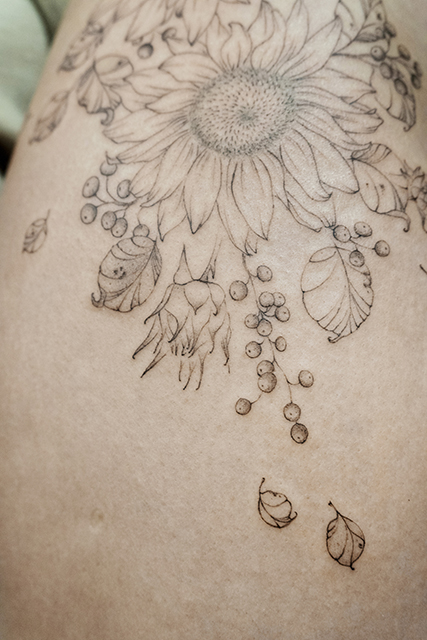 hip fineline flower tattoo with sunflower and berries made with dotwork from smasli ink an female tattoo artist working in salzburg austria