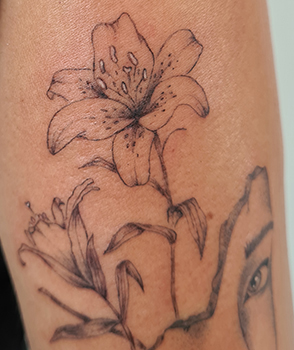 upper arm fineline flower tattoo with female head and a lily from smasli ink an female tattoo artist working in salzburg austria