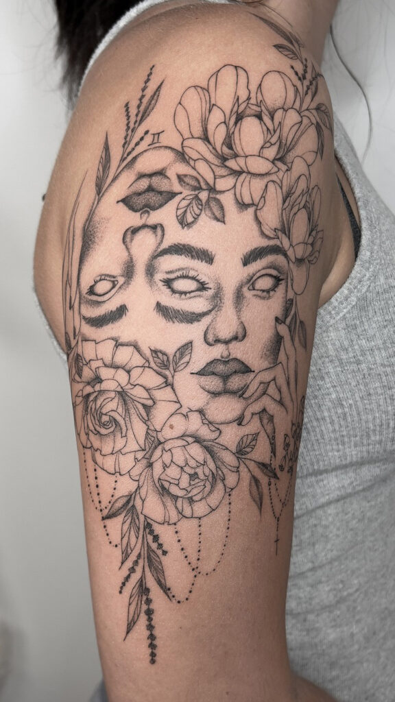 fineline flower tattoo upper arm with two lady heads and peonies from smasli ink an female tattoo artist working in salzburg austria